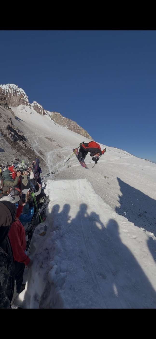 Cooper skiing in red and black above a snowy mountain