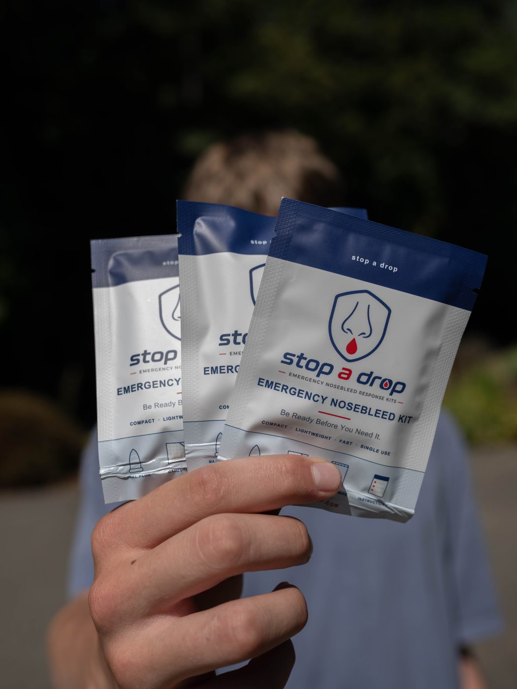 A Stop A Drop founder holding three Emergency Nosebleed Kits outdoors